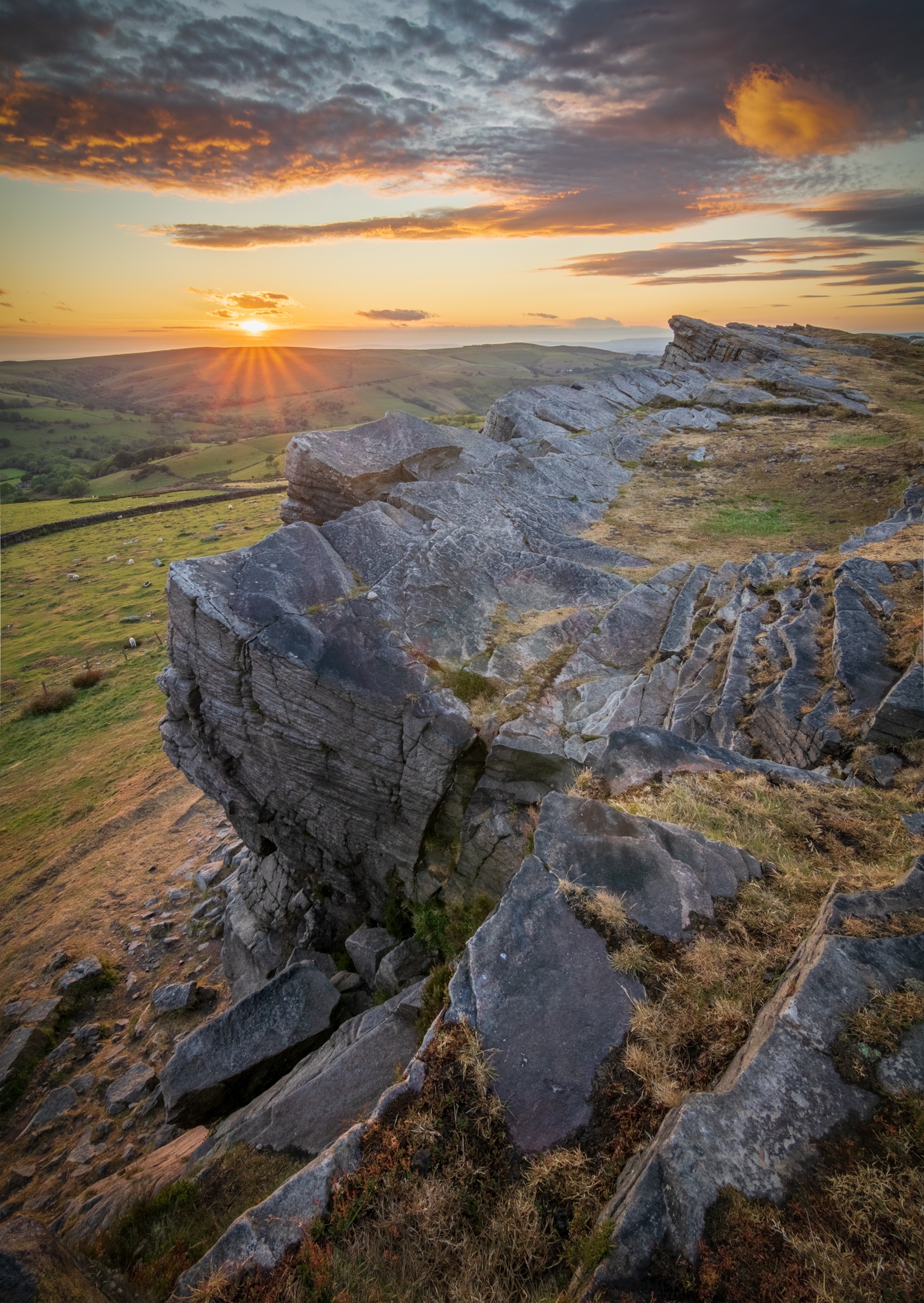 A vibrant sunset as the last rays of light catch the clouds above Windgather Rocks in the UK's Peak District National Park